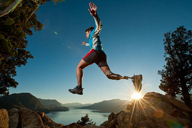 "Disabled man with prosthetic leg, jumping on a mountain with a beautiful backdrop and the sun setting."